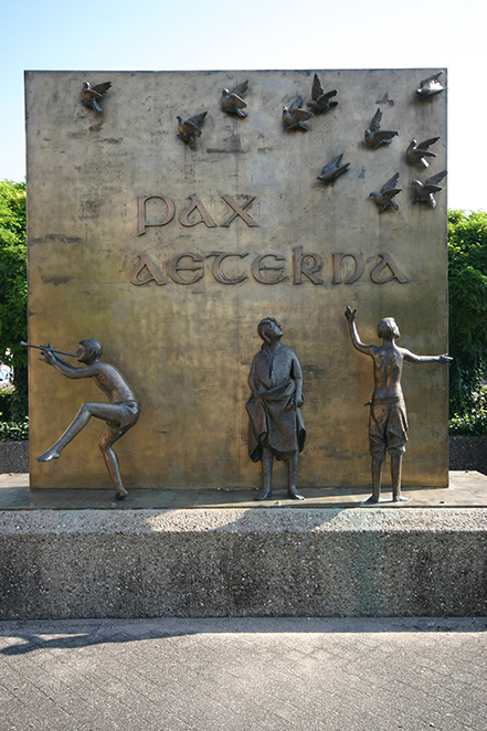 Wand mit dem Schriftzug "pax eterna" in die fliegende Tauben eingearbeitet sind. Davor stehen die Skulpturen von drei Kindern.